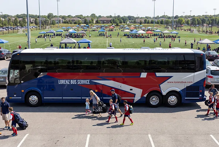 Lorenz Bus Service charter bus parked at a youth soccer tournament, with players and families walking alongside it