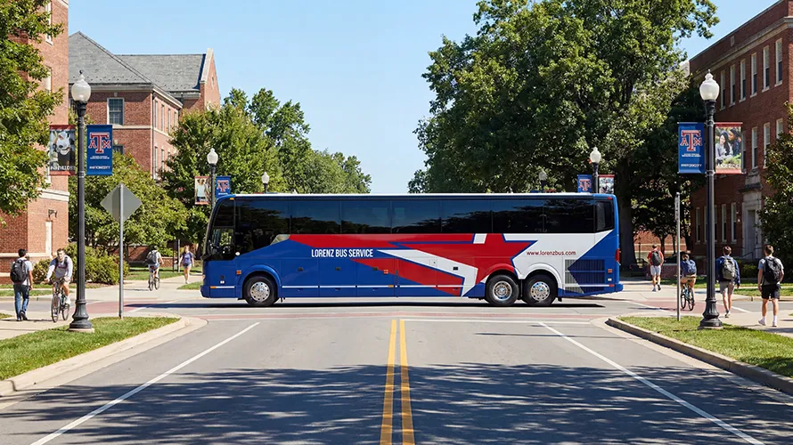 Lorenz Bus Service motorcoach crossing a campus street lined with brick buildings and Texas A&M University banners