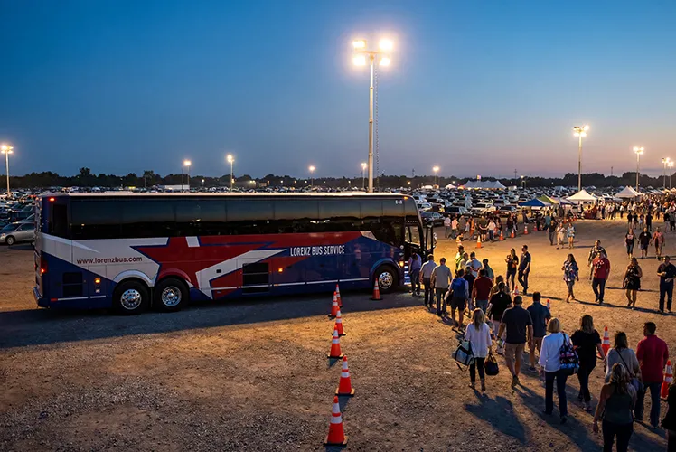 Lorenz Bus Service charter coach parked at a large outdoor event at dusk, with crowds of attendees boarding under stadium lights