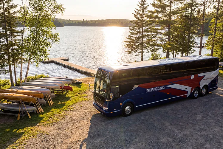 Lorenz Bus Service motorcoach parked lakeside at sunset, with canoes and a dock visible nearby