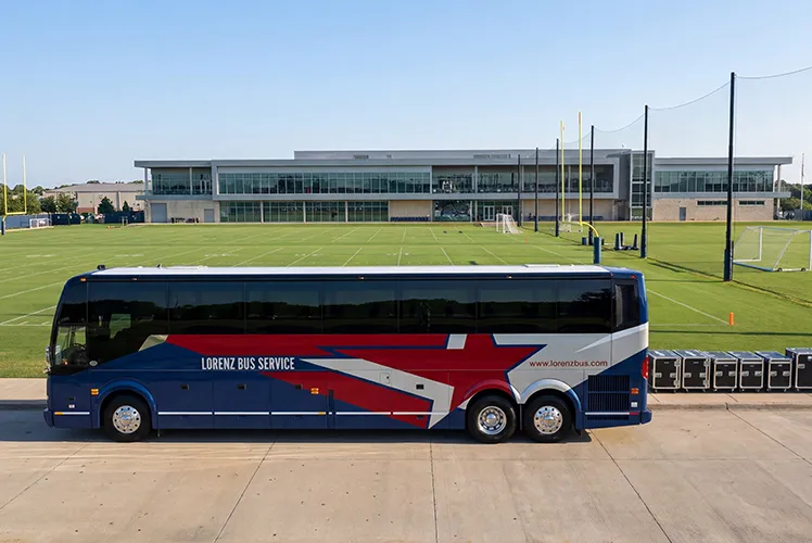 Lorenz Bus Service charter bus parked outside a collegiate athletic facility with football practice fields in the background