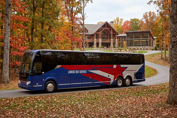 Lorenz Bus Service motorcoach parked outside a lodge surrounded by fall foliage