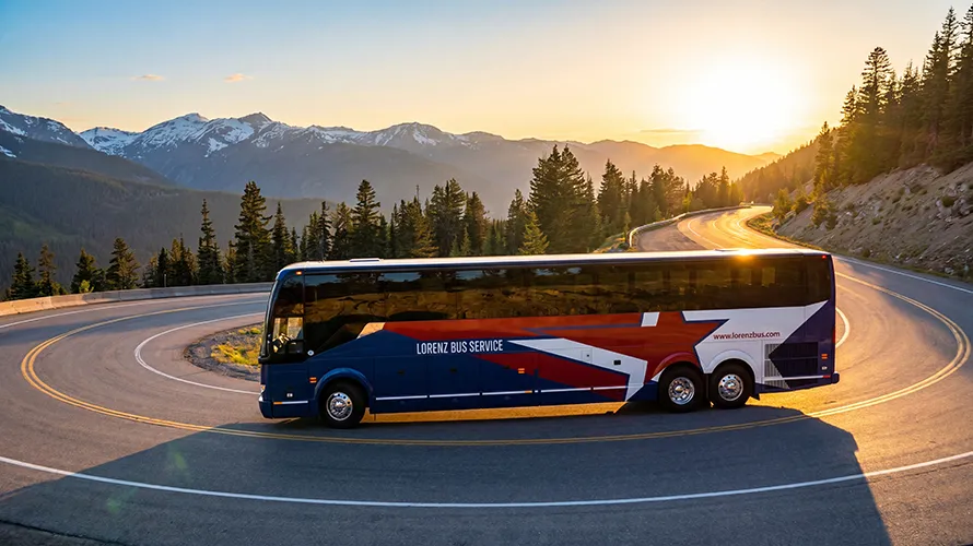 Lorenz Bus Service motorcoach on a winding mountain highway at sunset, with snow-capped peaks in the background
