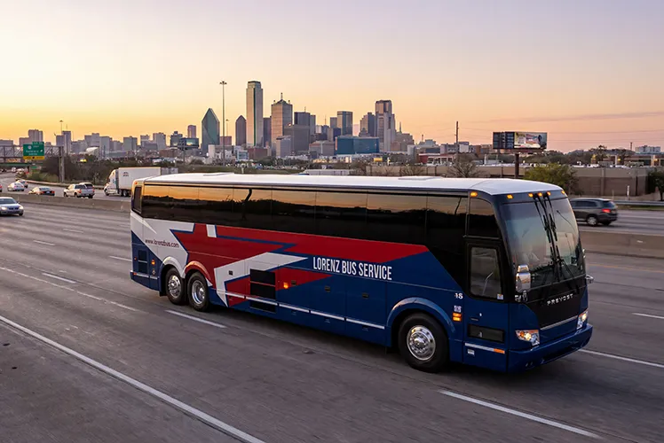 Lorenz Bus Service Prevost motorcoach traveling on a Dallas highway at sunset with the city skyline in the background