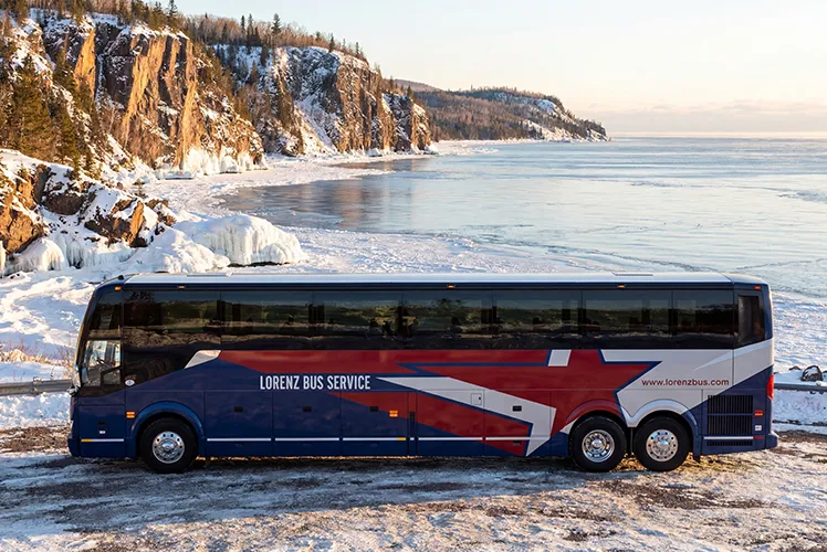 Lorenz Bus Service motorcoach parked along a snowy North Shore shoreline with frozen cliffs in the background
