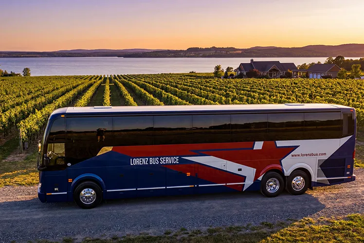 Lorenz Bus Service charter coach parked beside a vineyard and lake at sunset