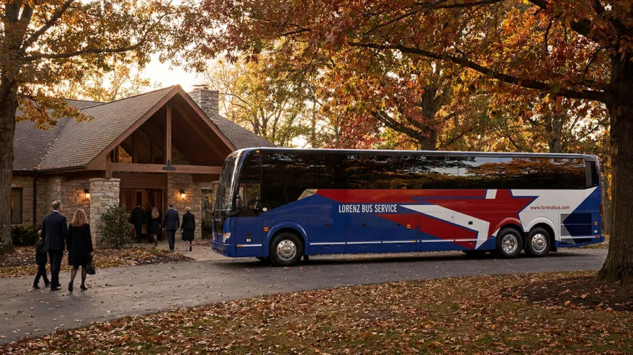 Lorenz Bus Service motorcoach parked outside a lodge entrance as passengers arrive on an autumn evening