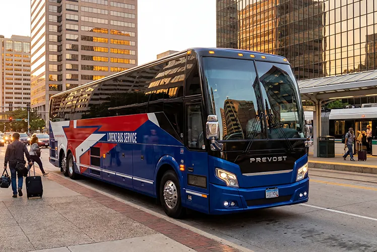 Lorenz Bus Service Prevost motorcoach parked at a downtown city stop as passengers board with luggage
