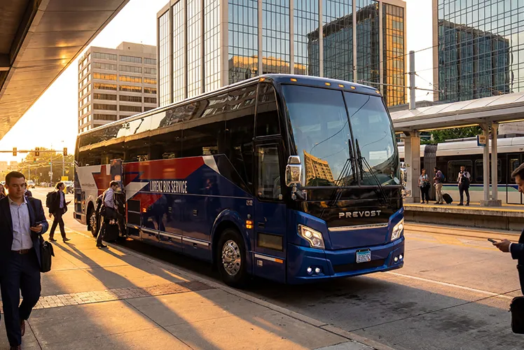 Lorenz Bus Service Prevost motorcoach parked at an urban transit station as passengers board at golden hour