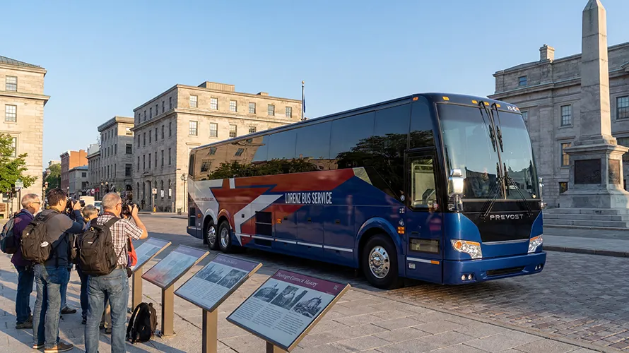 Lorenz Bus Service Prevost charter coach parked in a historic city square with photographers and informational plaques nearby
