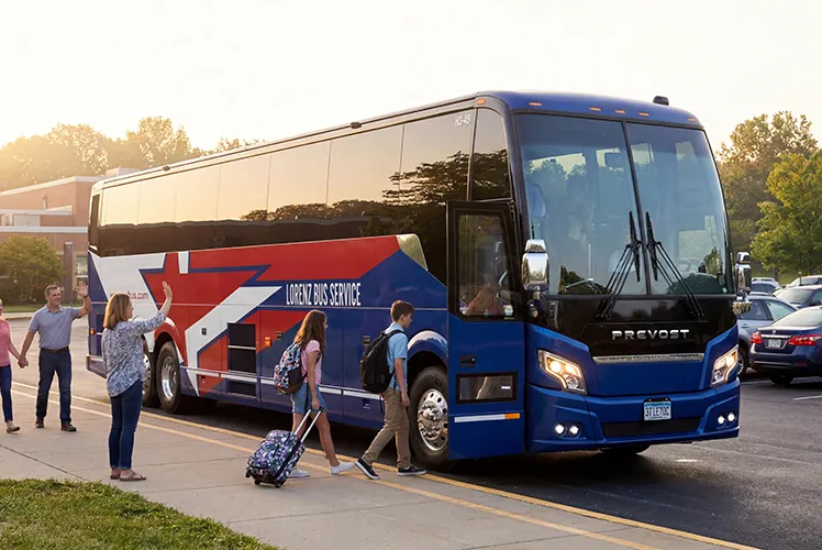 Students with luggage boarding a Lorenz Bus Service Prevost coach at sunset, with adults waving goodbye nearby