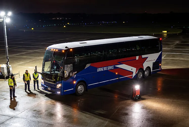 Lorenz Bus Service Prevost charter coach staged on a tarmac at night with crew members in safety vests standing nearby