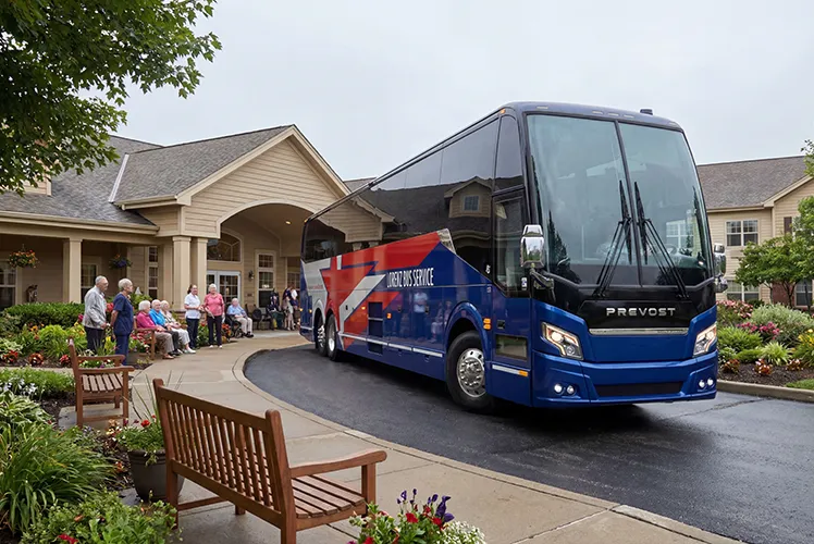 Lorenz Bus Service Prevost motorcoach parked at a senior living community entrance as a group of residents gathers outside
