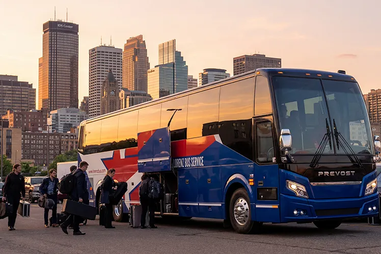 Passengers loading luggage onto a Lorenz Bus Service Prevost coach in downtown Minneapolis at sunset