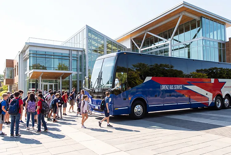 Students with backpacks boarding a Lorenz Bus Service motorcoach outside a modern school building