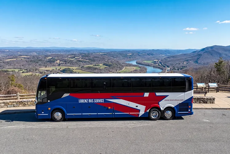 Lorenz Bus Service motorcoach parked at a scenic overlook with a river valley and rolling hills in the background