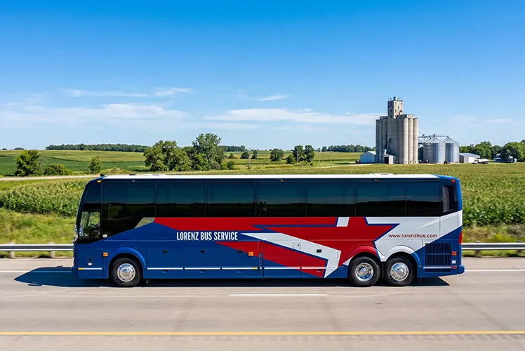 Lorenz Bus Service charter coach traveling along a Midwest highway past open farmland and grain silos