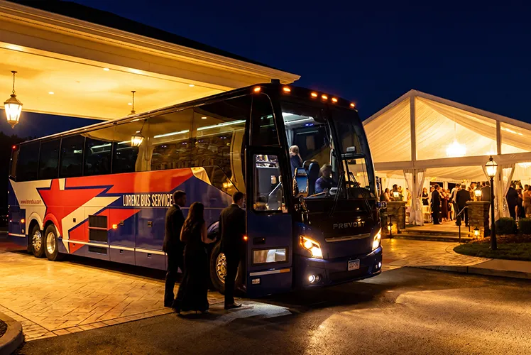 Formally dressed guests boarding a Lorenz Bus Service Prevost motorcoach outside an evening event venue with a lit tent nearby