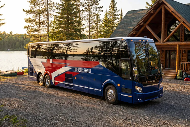 Lorenz Bus Service motorcoach parked outside a lakeside log cabin at sunset, ready for an outdoor excursion
