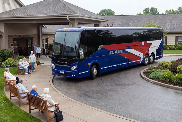 Lorenz Bus Service Prevost motorcoach pulling up to a senior living facility as residents wait on benches outside