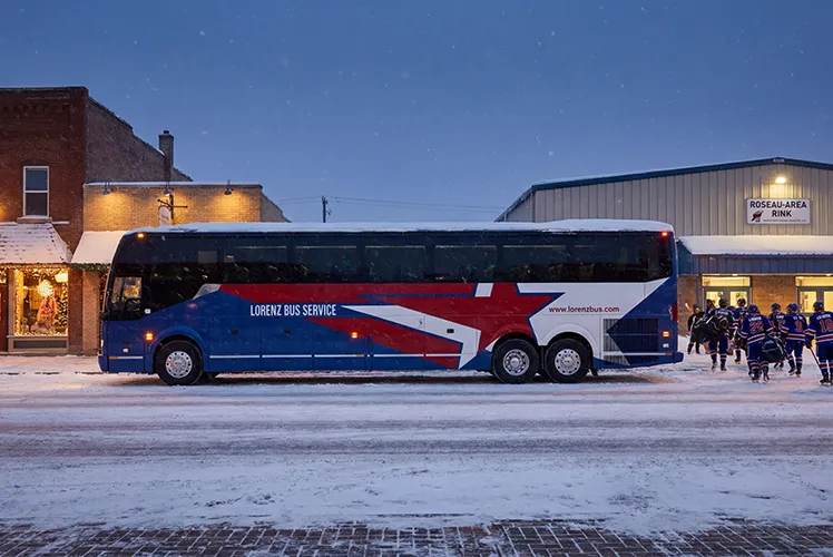 Lorenz Bus Service charter bus parked outside Roseau Area Rink in winter as hockey players board after a game