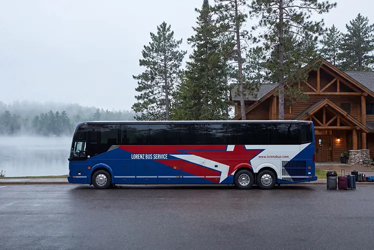 Lorenz Bus Service motorcoach parked outside a lakeside lodge, with luggage staged nearby on a misty morning