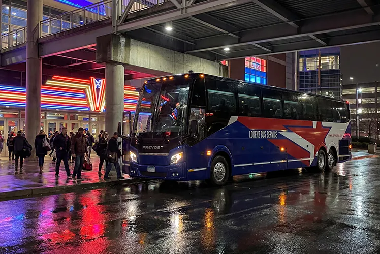 Lorenz Bus Service Prevost motorcoach loading passengers outside a lit arena entrance at night