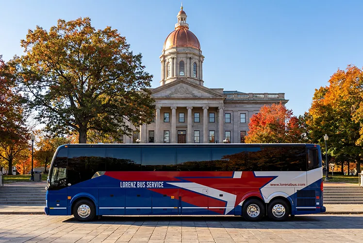 Lorenz Bus Service charter coach parked in front of a domed civic building surrounded by fall foliage