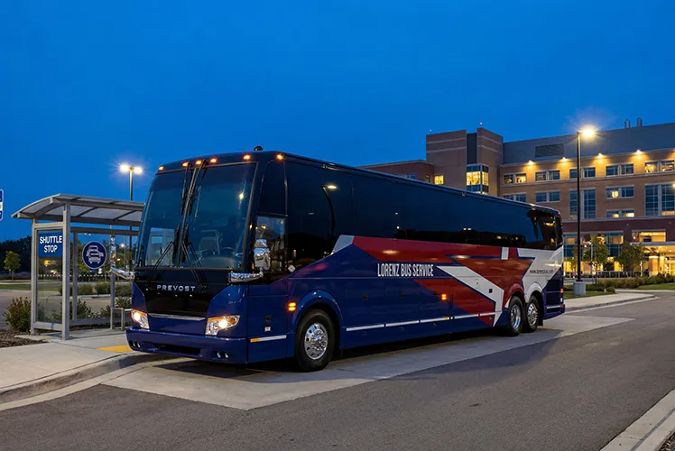 Lorenz Bus Service Prevost motorcoach parked at a shuttle stop outside a building at dusk
