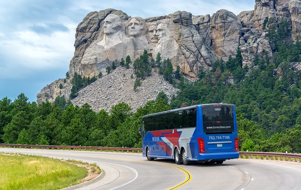 Lorenz Bus Service motorcoach traveling a winding road with Mount Rushmore in the background