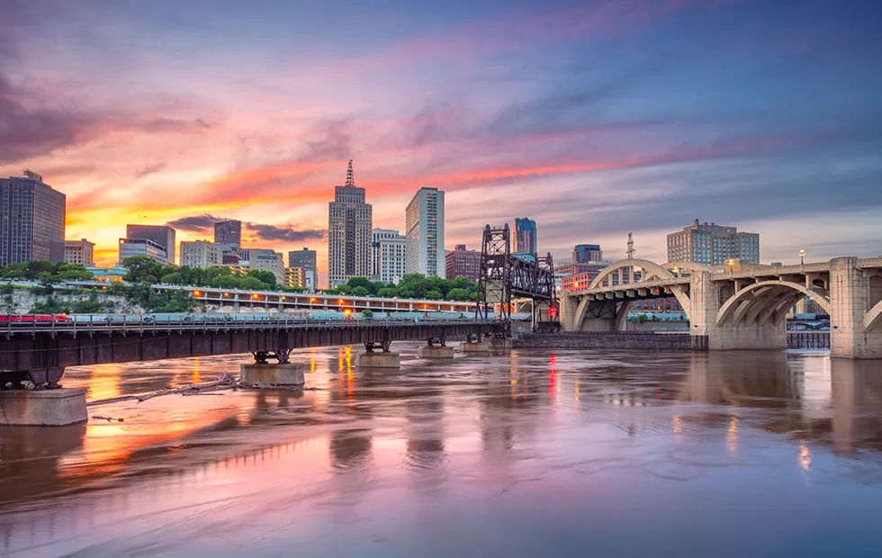 Saint Paul, Minnesota skyline at sunset reflected in the Mississippi River, with bridges in the foreground
