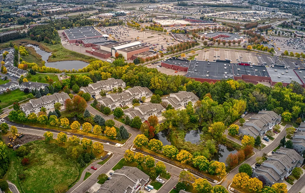 Aerial view of a Midwest suburban area with residential neighborhoods, tree-lined streets in fall color, and commercial buildings with large parking lots