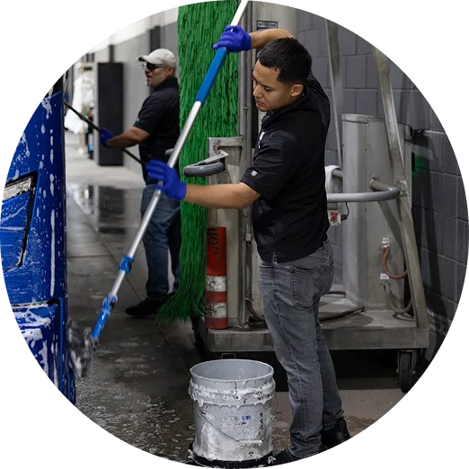 Two Lorenz Bus Service crew members in black uniforms washing and scrubbing a bus exterior with brushes and soapy water