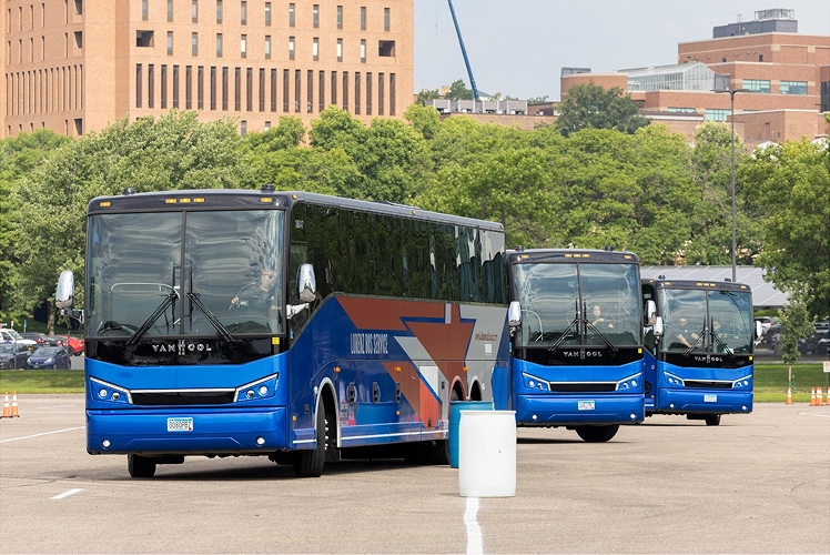 Three Lorenz Bus Service Van Hool coaches staged in a parking lot near a university campus, ready for departure