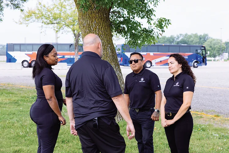 Four Lorenz Bus Service staff members in uniform discussing operations outdoors, with Lorenz coaches parked in the background